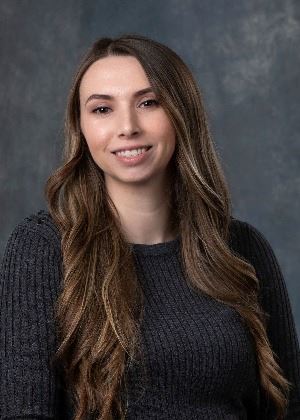 headshot of a female with long brunette hair and dark sweater